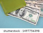 Hundred-dollar bills peek out of a green leather wallet on a turquoise background.