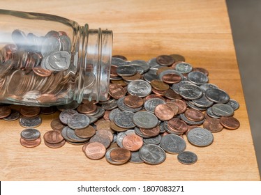 Hundreds Of US Coins Pouring Out Of Savings Jar On Wooden Table As Concept For Shortage Of Loose Change In USA