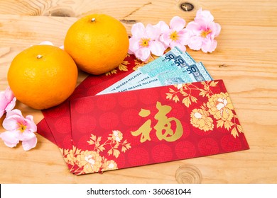 Hung Bao or red packet with Good Fortune Chinese character filled with Malaysia Ringgit currency, displayed with mandarin oranges