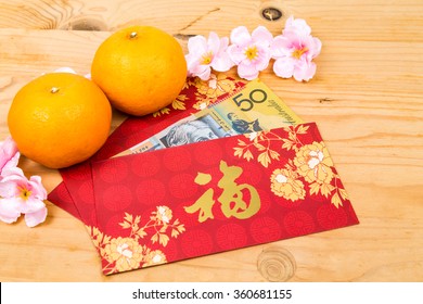 Hung Bao or red packet with Good Fortune Chinese character filled with Australian Dollar currency, displayed with mandarin oranges