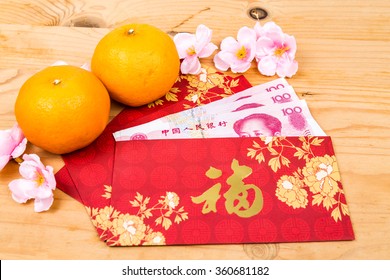Hung Bao or red packet with Good Fortune Chinese character filled with China Renminbi Yuan, displayed with mandarin oranges