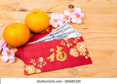 Hung Bao or red packet with Good Fortune Chinese character filled with US Dollar notes, displayed with mandarin oranges