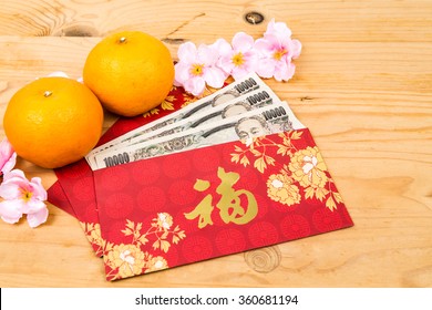 Hung Bao or red packet with Good Fortune Chinese character filled with Japanese Yen currency, displayed with mandarin oranges