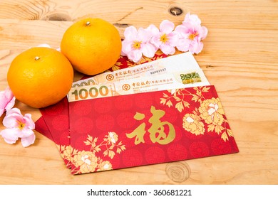 Hung Bao or red packet with Good Fortune Chinese character filled with Hong Kong Dollars, displayed with mandarin oranges
