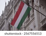 The Hungarian flag is flying in the wind at the historic Neo-Gothic facade of the Hungarian parliament in Budapest, Hungary.