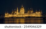 The Hungarian Parliament Building is beautifully illuminated against the night sky, reflecting in the Danube River. This architectural masterpiece in Budapest showcases Gothic Revival style.