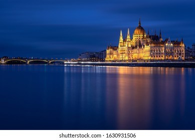 Hungarian Parliament Building built in the Gothic Revival style in Budapest viewed at night with Danube river and Margit bridge. Long exposure.