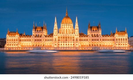 Hungarian Parliament building illuminated at night on the banks of the Danube river in central Europe. Passing boats are blurred in the reflection of the building. - Powered by Shutterstock