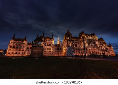 The Hungarian Parliament On A Winter Night Illuminated, With The National Christmas Tree Lighted Up In Front. Budapest, Hungary