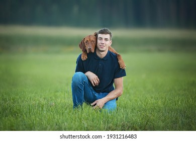 The hungarian vizsla dog snuggles up to his owner. Outdoor portrait of young man and his dog