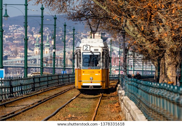 Hungary, Budapest: Street view with famous historic\
orange tram cable car in the city center of the Hungarian capital\
with cityscaepe and blue sky in the background - travel history.\
Feb 06, 2019