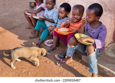 Hungry African Children Eating Porridge In Front Of The House In The Village, Puppy Watching