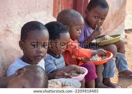 hungry African children eating porridge in front of the house in the village