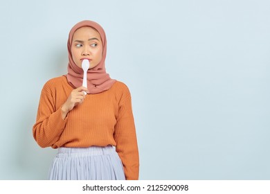 Hungry Beautiful Asian Woman In Brown Sweater Holding Spoon In Mouth Think Of Tasty Food Isolated Over White Background