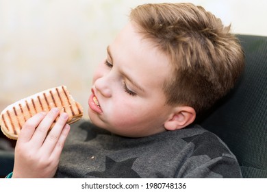 A Hungry Boy Eating A Hot Dog At Home Kid Eats A Hot-dog Sandwich.Indoors Shot.Closeup.