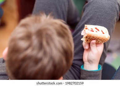 A Hungry Boy Eating A Hot Dog At Home Kid Eats A Hot-dog Sandwich.Indoors Shot.Closeup.