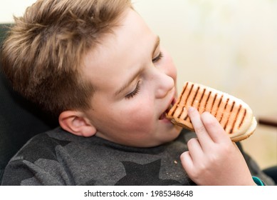 A Hungry Boy Eating A Hot Dog At Home Kid Eats A Hot-dog Sandwich.Indoors Shot.Closeup.