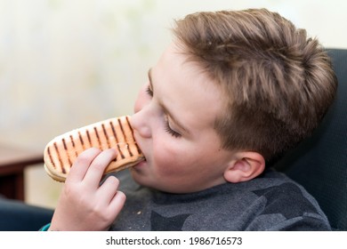 A Hungry Boy Eating A Hot Dog At Home Kid Eats A Hot-dog Sandwich.Indoors Shot.Closeup.