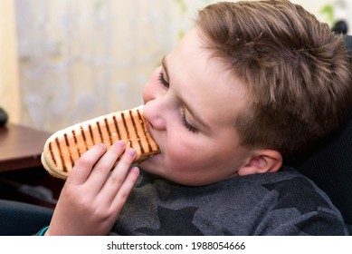 A Hungry Boy Eating A Hot Dog At Home Kid Eats A Hot-dog Sandwich.Indoors Shot.Closeup.