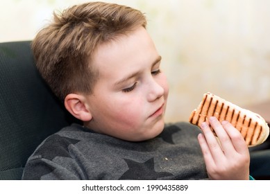 A Hungry Boy Eating A Hot Dog At Home Kid Eats A Hot-dog Sandwich.Indoors Shot.Closeup.