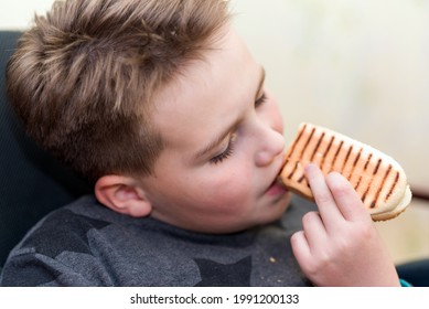 A Hungry Boy Eating A Hot Dog At Home Kid Eats A Hot-dog Sandwich.Indoors Shot.Closeup.