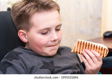 A Hungry Boy Eating A Hot Dog At Home Kid Eats A Hot-dog Sandwich.Indoors Shot.Closeup.