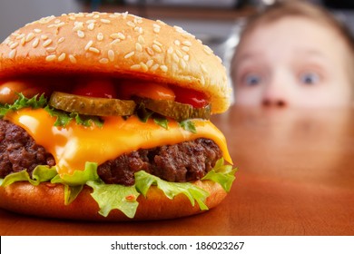 Hungry boy is staring and smelling a burger on wooden table