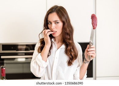 Hungry Brunette Woman Cooking And Eating Red Meat Steak With Glass Of Red Wine. Housewife Concept