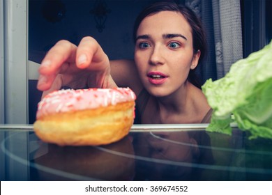 Hungry Cute Woman Reaches For Donut At Night Near Fridge