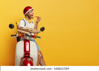 Hungry Delivery Driver Stops On Road, Eats Tasty Pizza, Has Temptation, Sits On Motorcycle, Being In Good Mood After Delicious Snack, Isolated On Yellow Background, Free Space Right. Time For Dinner