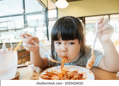 Hungry Face And Enjoy Eating Concept.Little Asian Girl Enjoy Eating With Spaghetti Bolognese With Cheese On A Plate In Lunch Time At Restaurant.