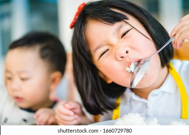 Hungry Face And Enjoy Eating Concept.Little Asian Girl Enjoy Eating With Rice And Vegetable On A Plate In Lunch Time At Home.Asian Kid Girl Holding Spoon With White Rice And Open Her Mouth.