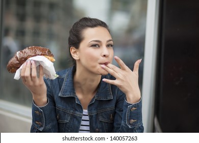  hungry girl eating a donut with chocolate and sucking her finger
