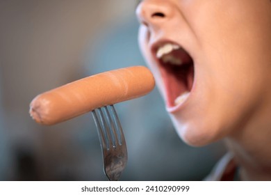 hungry girl with an open mouth eats a sausage from a fork. Delicious fast junk food. Close-up.
