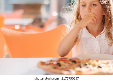Hungry kid girl eating pizza on cafe terrace on sunny day. outside restaurant copy space