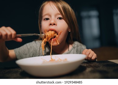 Hungry Little Girl Appetite Eating The Bolognese Pasta Reeling Up It On The Fork And Putting To Mouth In The Low Light Kitchen Table. 