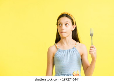 Hungry little girl with cravings savoring her next meal. Charming preteen girl holding a fork to start eating lunch and thinking about her favorite food