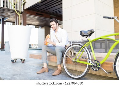 Hungry male executive having sandwich while sitting on bench by bike