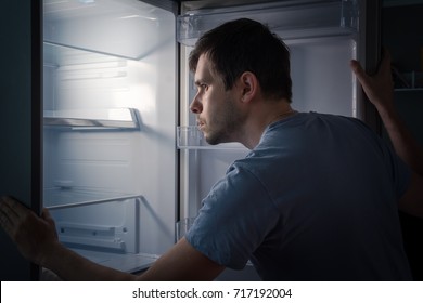 Hungry Man Is Looking For Food In Empty Fridge At Night.