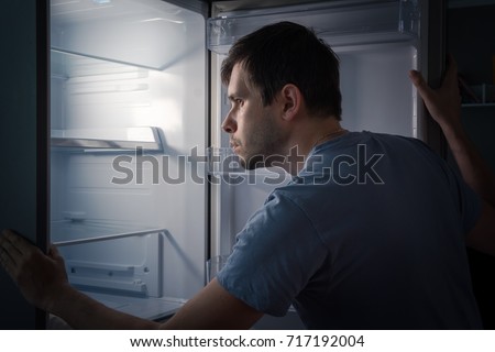 Hungry man is looking for food in empty fridge at night.