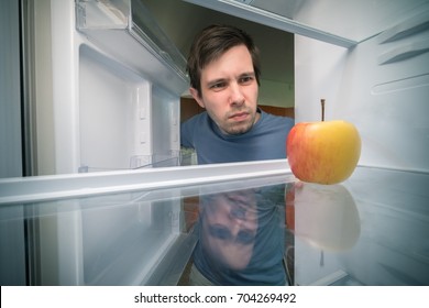 Hungry Man Is Looking For Food In Fridge. Only Apple Is Inside Empty Fridge.