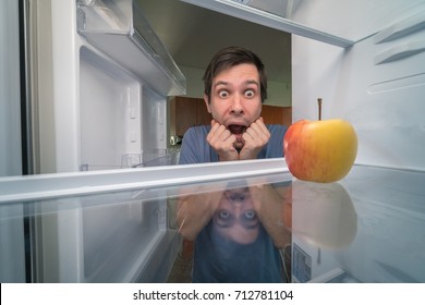 Hungry Man Is Looking For Food In Fridge And Is Shocked. Only Apple Is Inside Empty Fridge.