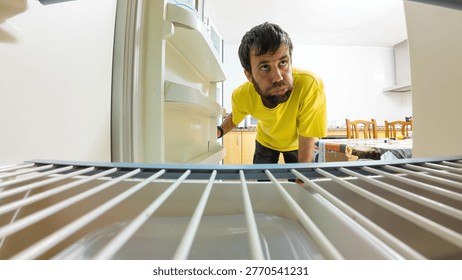 Hungry man looking inside empty refrigerator for food