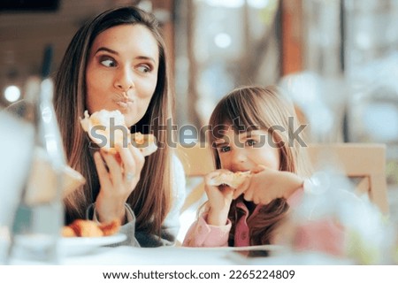 
Hungry Mom and Daughter Having Pizza in a Restaurant. Happy family craving for fast food meal

