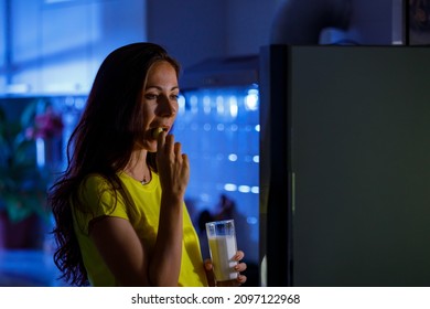 Hungry Pregnant Female Opening Refrigerator And Eating And Drinking Late At Night While Stroking Belly In Dark Kitchen