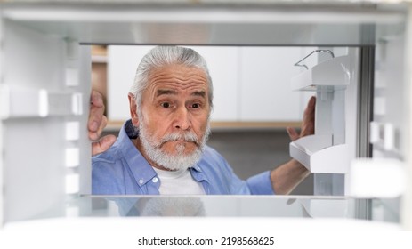 Hungry Senior Man Looking At Empty Shelves In Fridge At Home, Upset Elderly Gentleman Searching For Food In Refrigerator, Old Male Suffering Financial Crisis And Absence Of Money, View From Inside