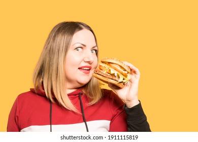 A hungry woman is biting a big tasty burger. . Unhealthy food