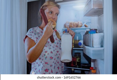 Hungry Woman Eating Food From The Open Refrigerator At Night.Late Overeating Causing By The Stress At Home.Hormones In Menopause And Eating Concept.Glutton Woman Eating From Fridge