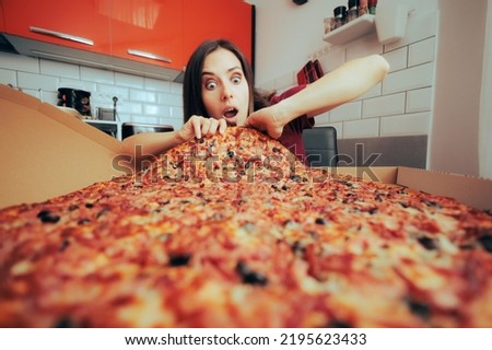 
Hungry Woman Eating a Large Pizza by Herself in the Kitchen. Girl craving for a huge portion of Italian delicious dish 
