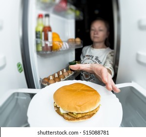 Hungry woman eating at night near refrigerator